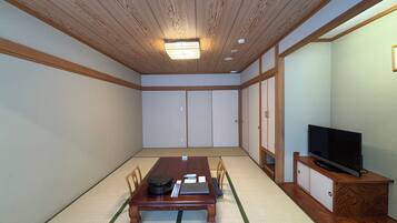Um quarto japonês tradicional com tatames, teto de madeira baixo, portas deslizantes e uma televisão sobre suporte de madeira.