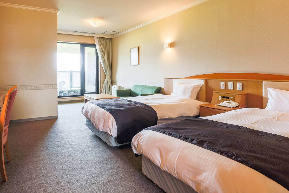 Une chambre d’hôtel avec deux lits, une chaise, une petite table et une fenêtre avec des rideaux.