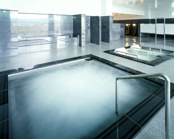 Una piscina interior moderna con agua cristalina, barandillas de metal y vistas de la ciudad a través de amplias ventanas.