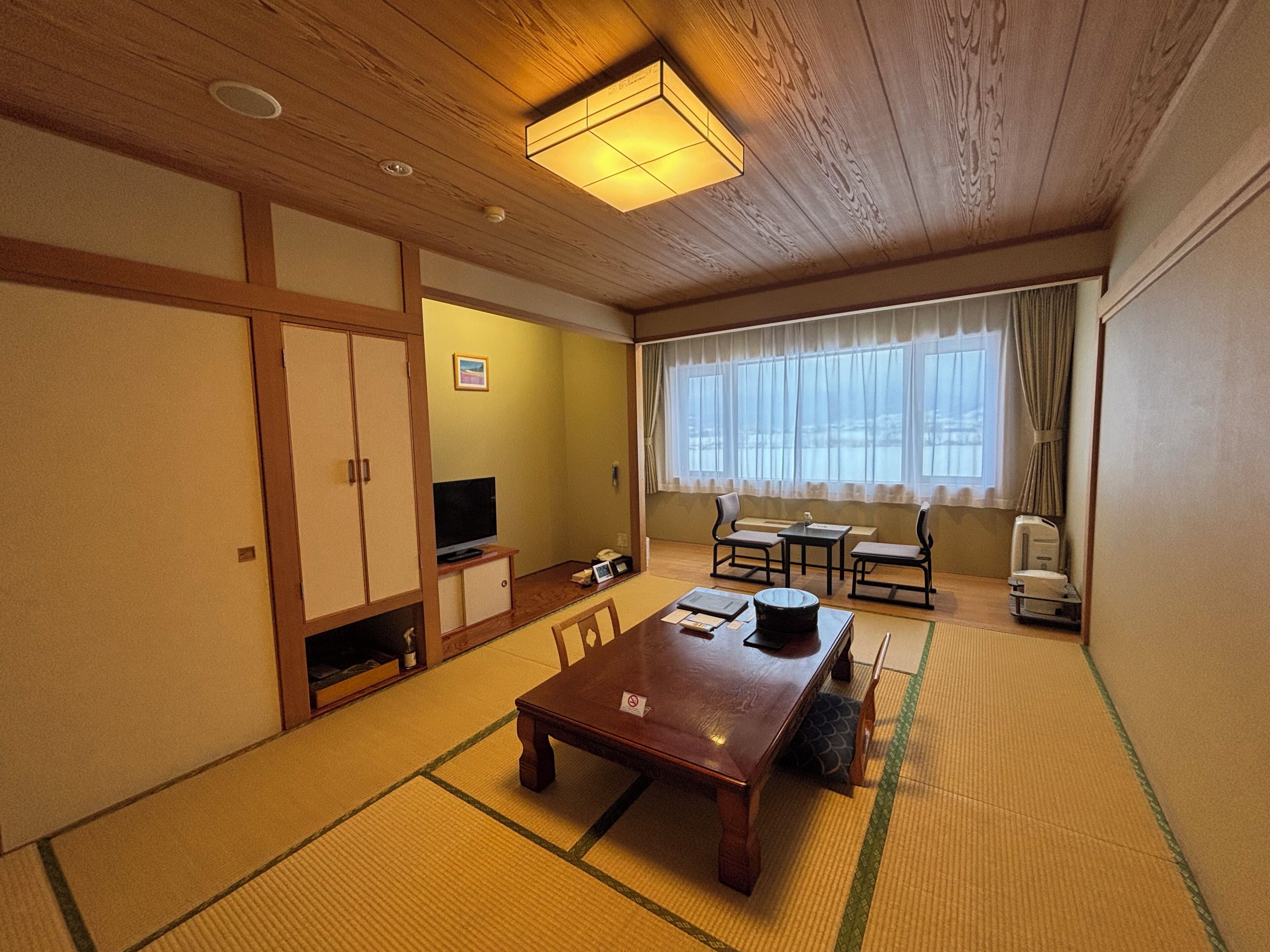 A traditional Japanese-style room with tatami flooring, a low wooden table, a television, and a sliding door.