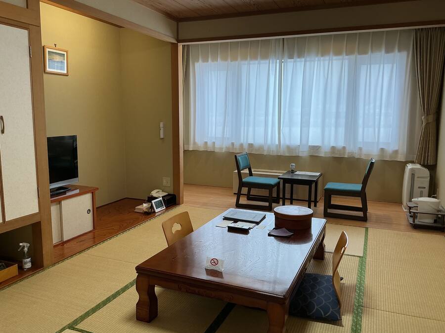 Um quarto japonês tradicional com tatames, uma mesa de madeira, uma televisão e um futon.