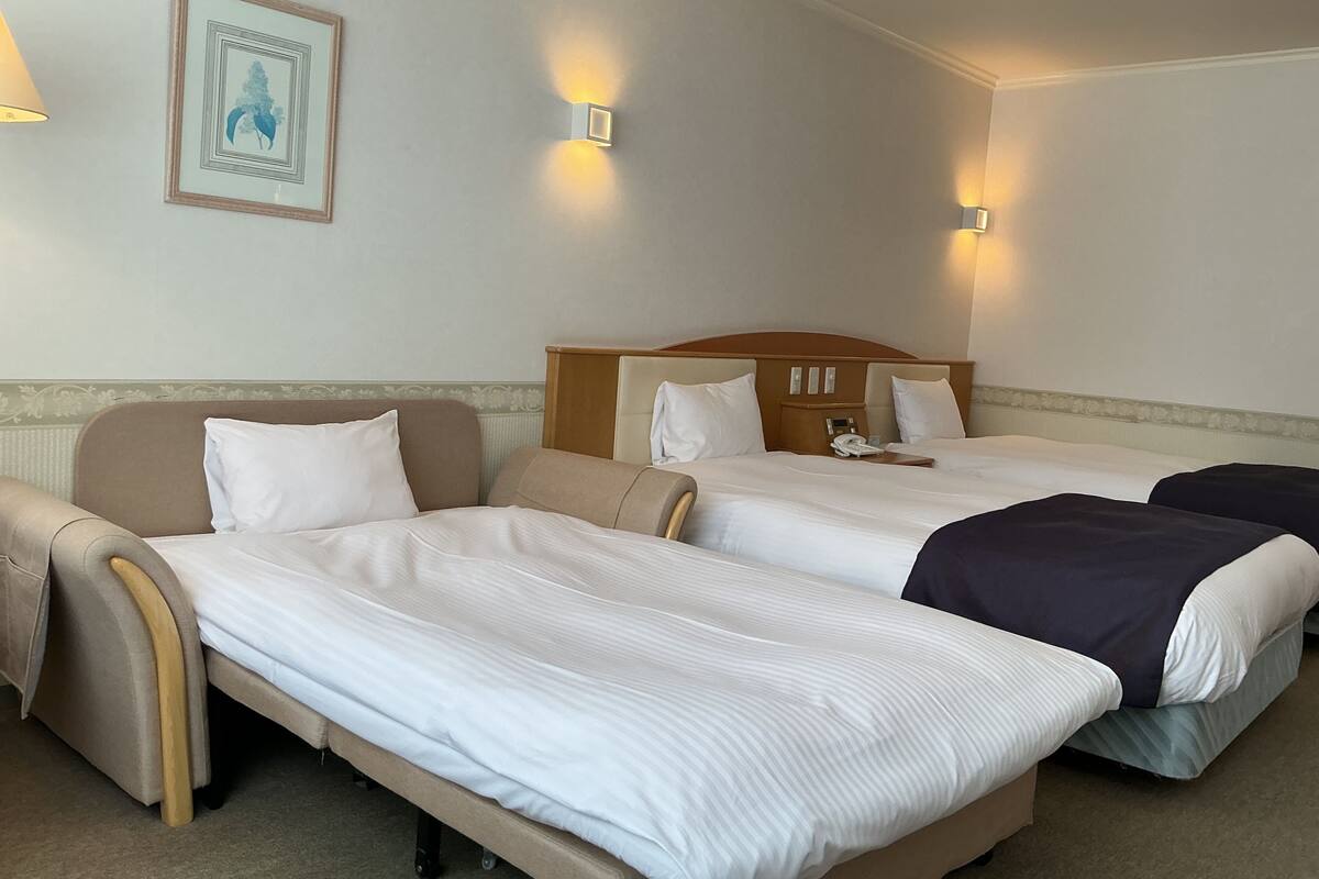 Une chambre d’hôtel avec deux lits simples, une tête de lit en bois, une table de chevet avec un téléphone et un tableau encadré au mur.