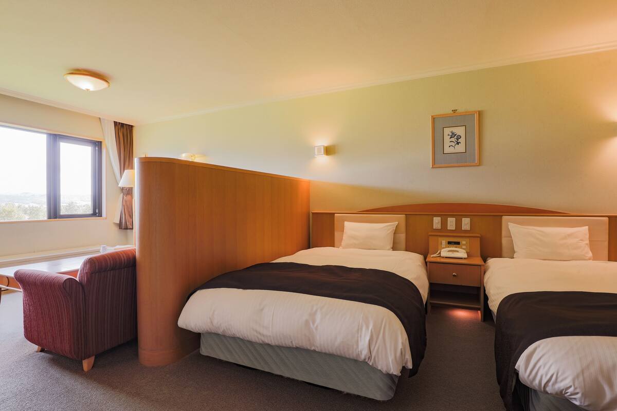 Une chambre d’hôtel avec deux lits, un bureau, une chaise et une fenêtre avec des rideaux.