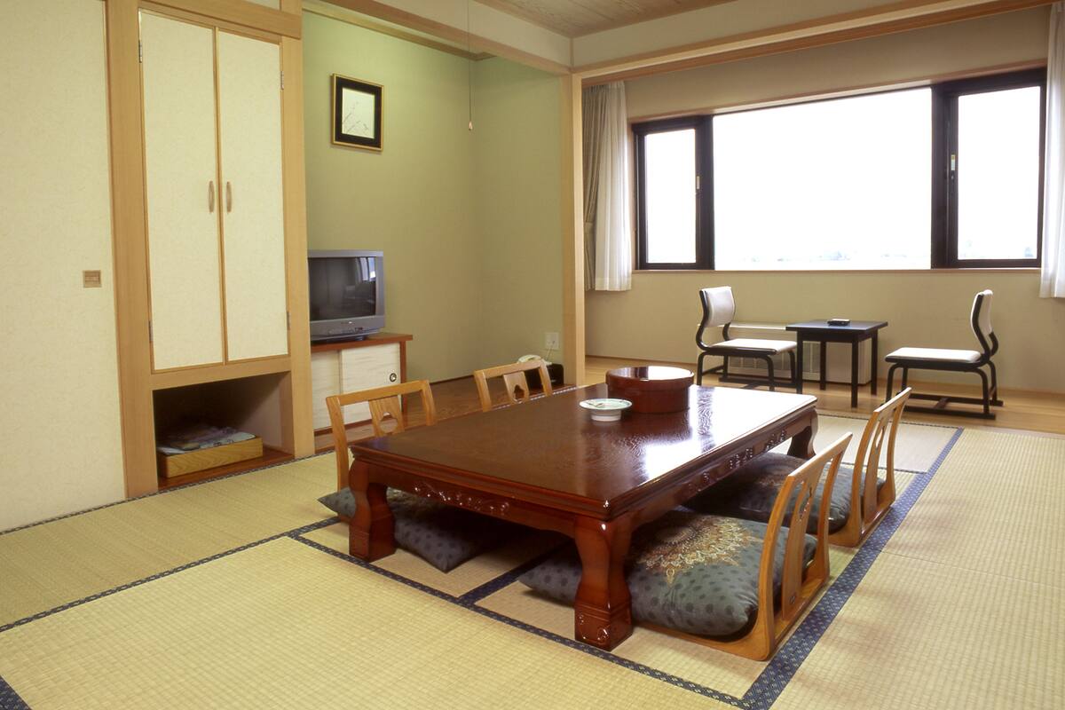 Une pièce de style japonais traditionnel, avec un sol recouvert de tatamis, une petite table en bois et un téléviseur posé sur un meuble.