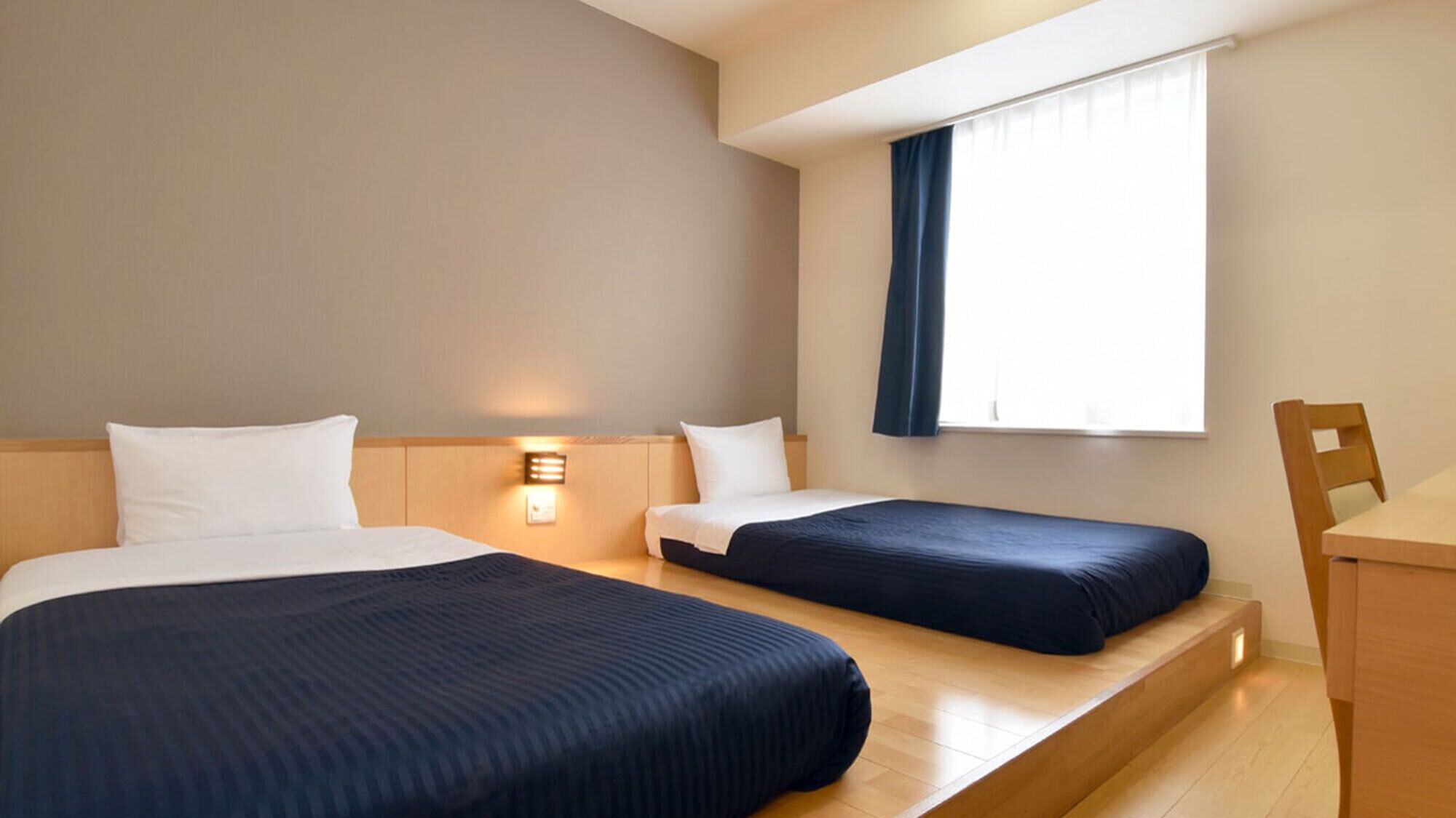 Ein Hotelzimmer mit zwei Betten, einem Schreibtisch und einem Fenster mit Vorhängen.