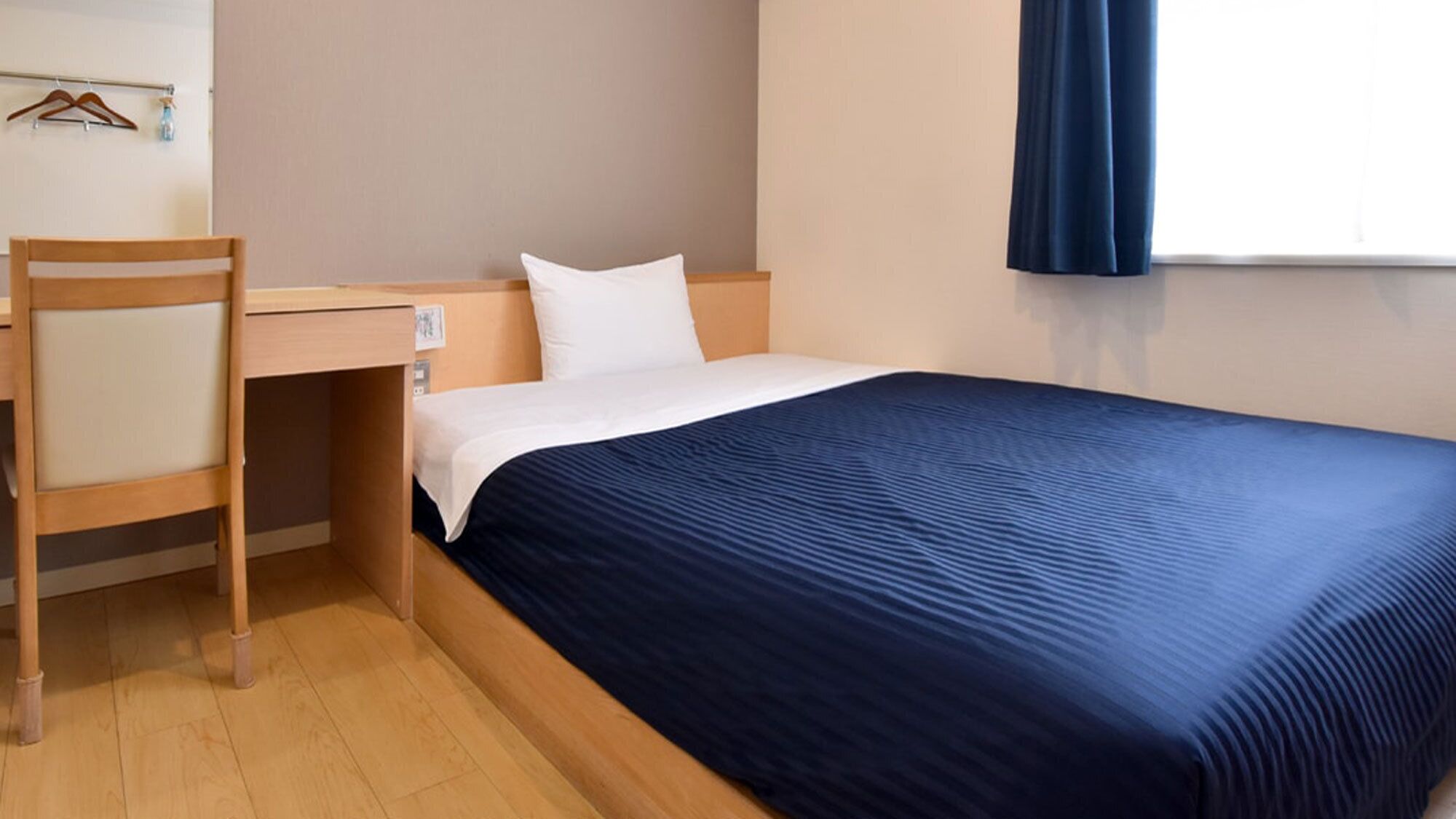 A hotel room with a bed, a desk, a chair, and a window with curtains.