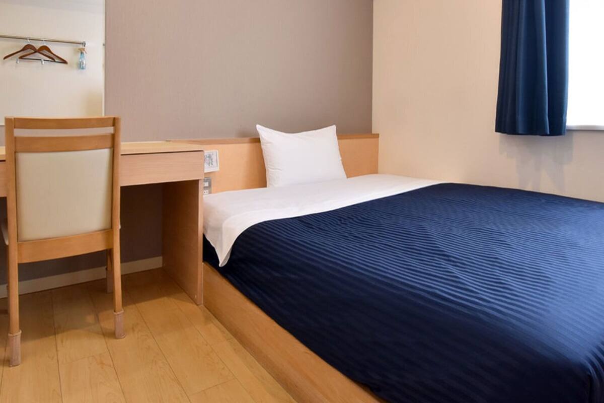 Una habitación de hotel con cama, escritorio, silla y ventana con cortinas.