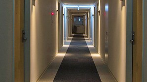 Een hotelgang met deuren aan beide kanten, een geruit tapijt en een rood bord met de tekst ‘uitgang’.