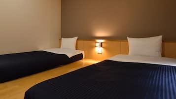 A hotel room with two single beds, wooden flooring, a wall-mounted light fixture, and a plain wall.