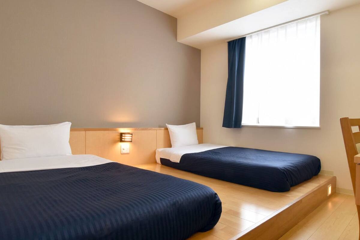 Una habitación de hotel con dos camas, un escritorio y una ventana con cortinas.