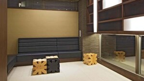 A modern interior with a dark sofa, wooden stools, and a glass partition. - Iwamizawa Hotel 5 Jo (Iwamizawa)