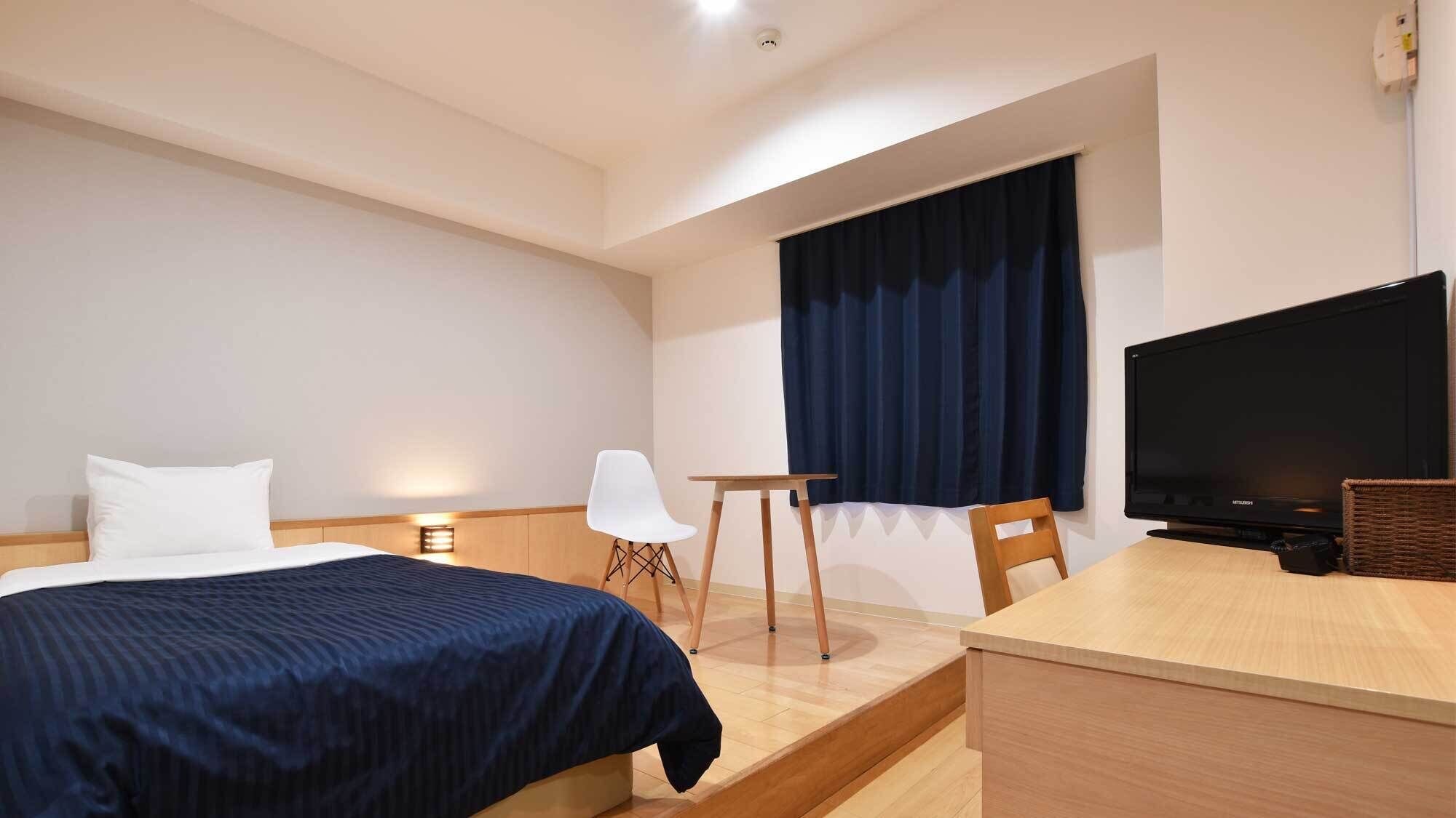 Ein Hotelzimmer mit einem Bett, einem Schreibtisch, einem Stuhl, einem Fernseher und einem Fenster mit Vorhängen.