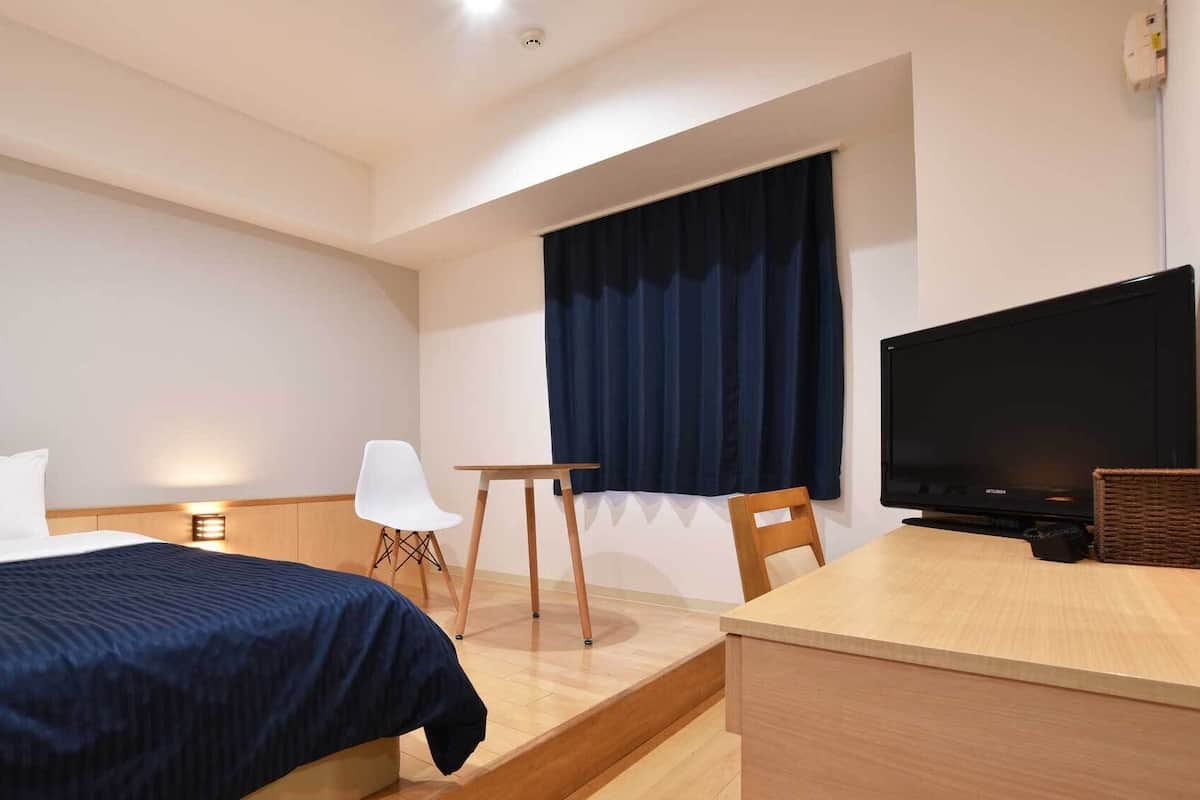 A hotel room with a bed, a desk, a chair, a television, and a window with curtains.