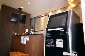 A self-service kiosk with a screen, card reader, and cash dispenser, located in a room with wooden paneling and a television mounted on the wall. - Iwamizawa Hotel 5 Jo (Iwamizawa)