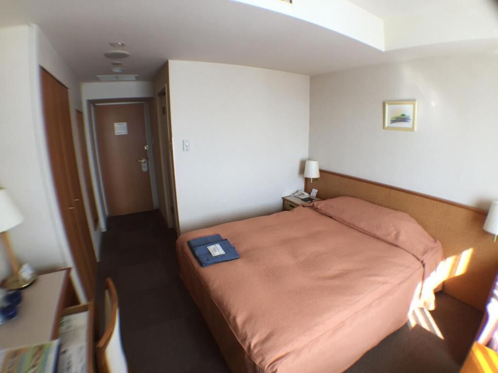 A hotel room with a single bed, a nightstand with a lamp, a small table with a lamp, and a door leading to another room.