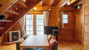 A cozy cabin interior with a wooden interior, a dining table, a sofa, a flat-screen TV, and a fireplace. - Niseko Hirafu Izumikyo Rental Cottage (Kutchan)
