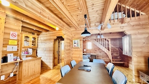 A wooden cabin interior with a dining table, chairs, a staircase, and a no-smoking sign. - Niseko Hirafu Izumikyo Rental Cottage (Kutchan)