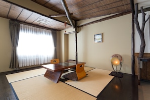 A traditional Japanese room with tatami flooring, a low wooden table, and a ceiling fan.