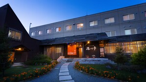 A modern building with a well-lit entrance, a stone pathway, and a garden with orange flowers. - Niseko Annupuri Onsen Yugokorotei (Niseko)