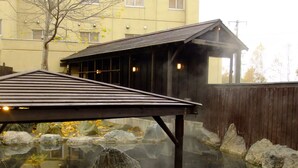 A traditional Japanese-style building with a wooden structure and a tiled roof, situated over a reflective water body with rocks and a wooden fence in the background. - Niseko Annupuri Onsen Yugokorotei (Niseko)