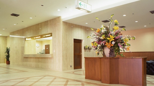 A hotel reception area with a reception desk, a potted plant, and a sign indicating the direction to the exit. - Hotel North City (Sapporo)