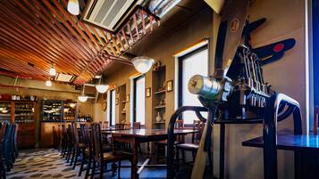 A restaurant interior with wooden ceiling beams, hanging pendant lights, a bar area with shelves of bottles, and a large mechanical sculpture.