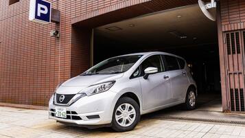 Un Nissan platejat estacionat davant d'un edifici amb un senyal de pàrquing.