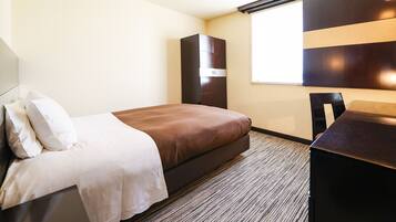 Una habitació d'hotel amb un llit, una taula de treball i un armari.