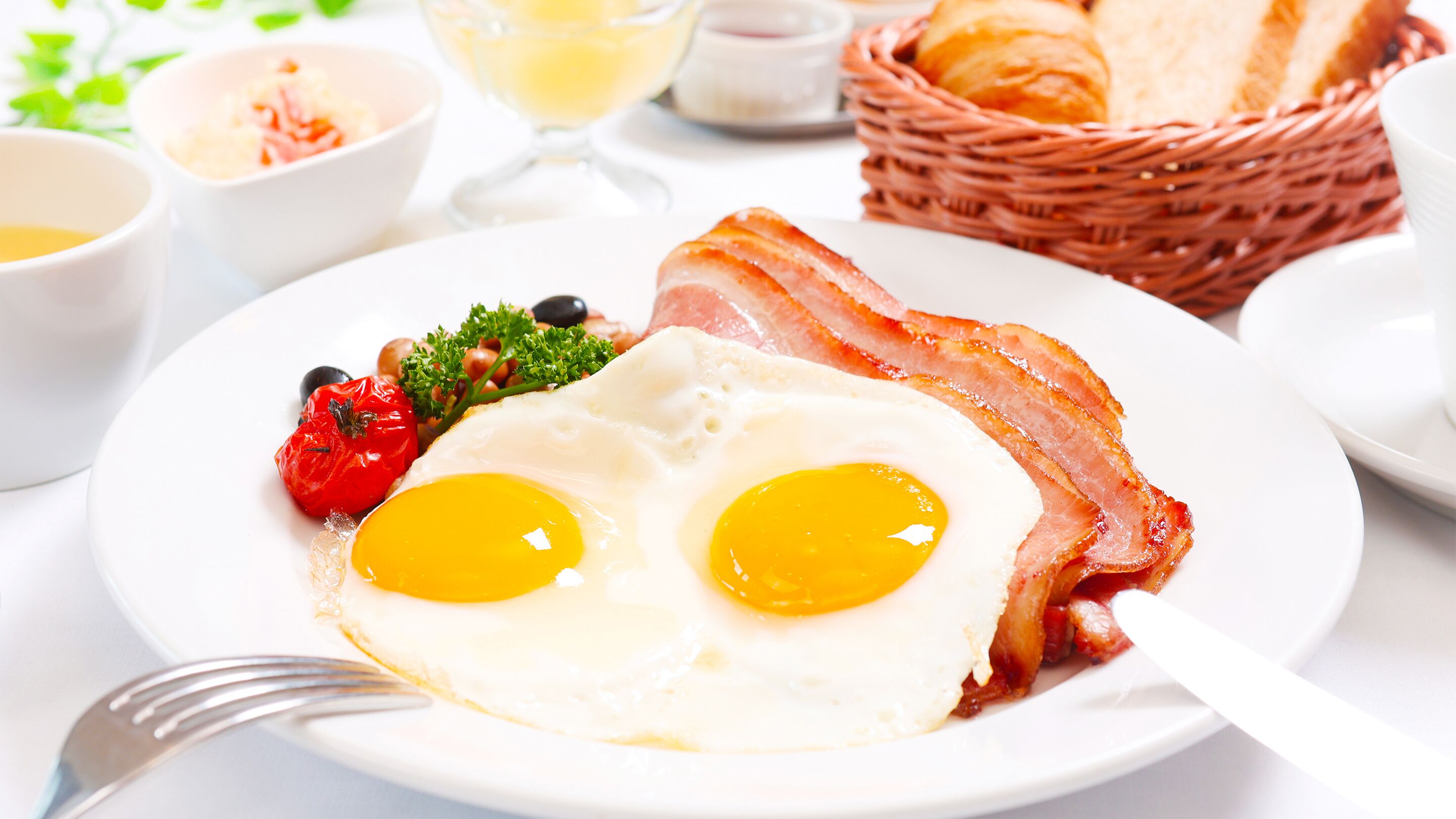 Un plato de desayuno con huevos, tocino, tomates y verduras de hoja.