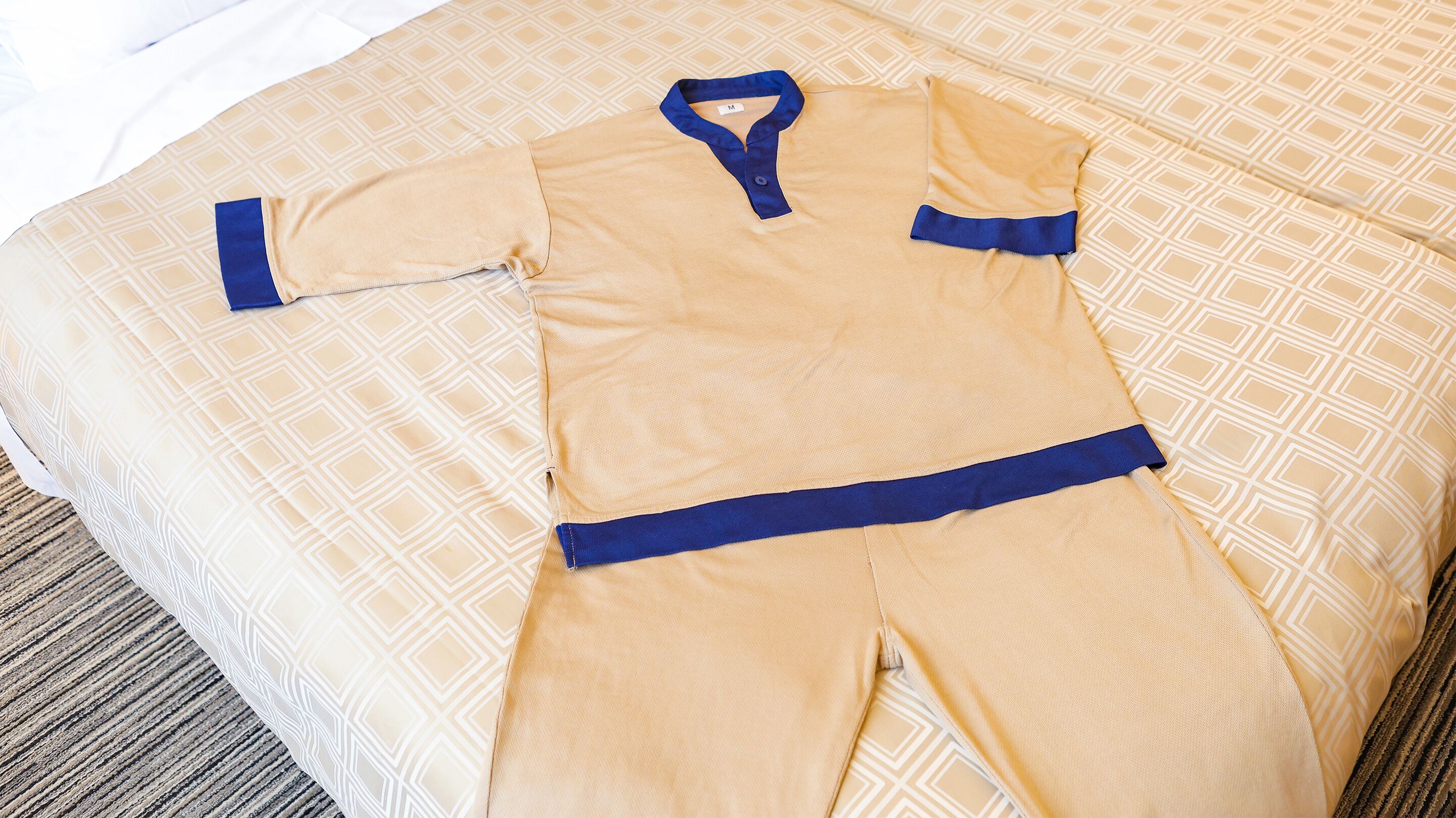 A neatly arranged bed with a patterned bedspread and a matching set of pajamas laid out on it.