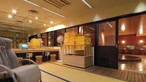 A modern hotel lobby with a reception desk, seating area, and a stack of yellow towels. - Obihiro Tennen Onsen Fukui Hotel (Obihiro)