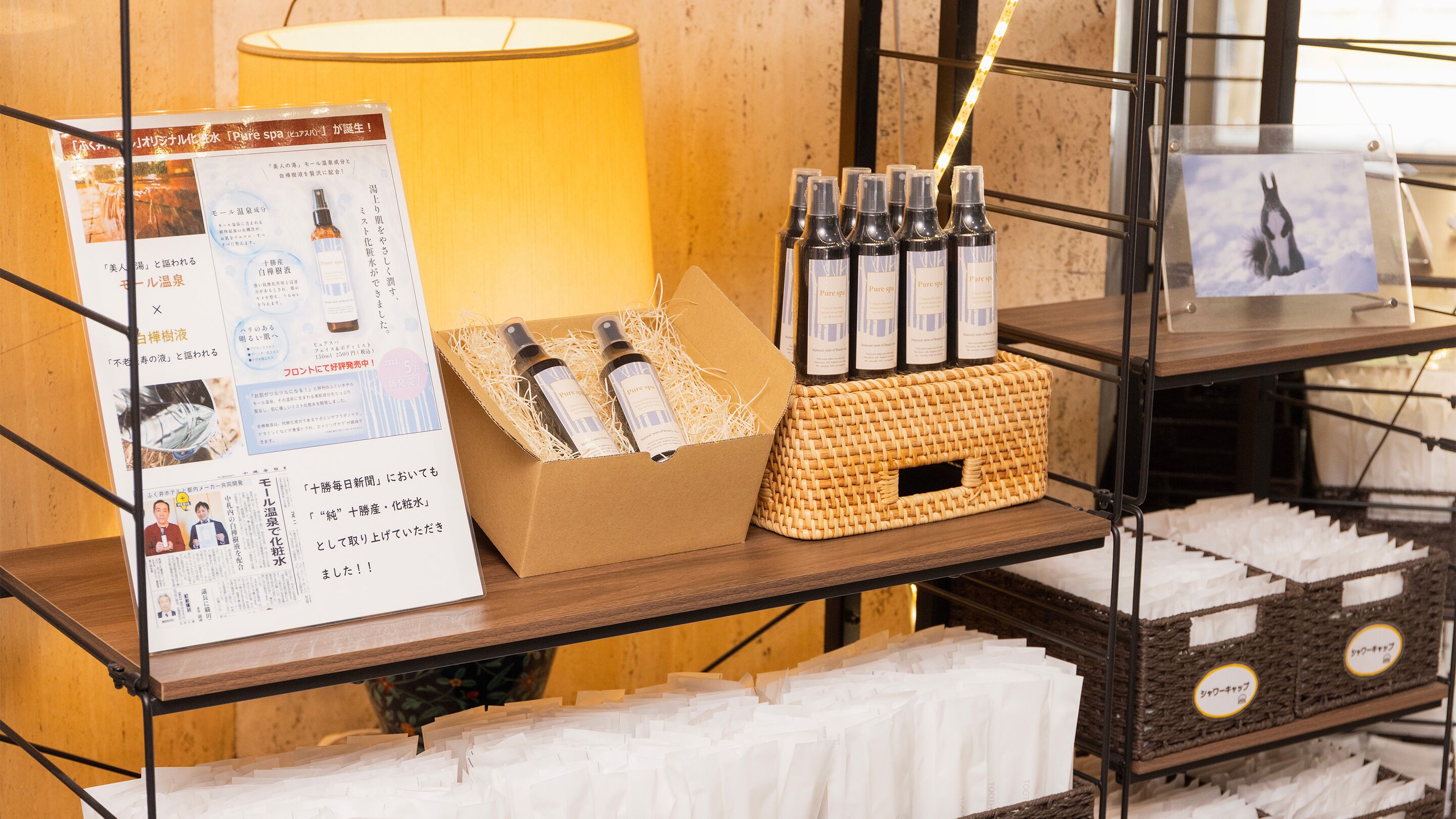 Ausstellung von Wellnessprodukten, darunter Flaschen und eine Schachtel, mit Informationspostern und einer Lampe im Hintergrund.
