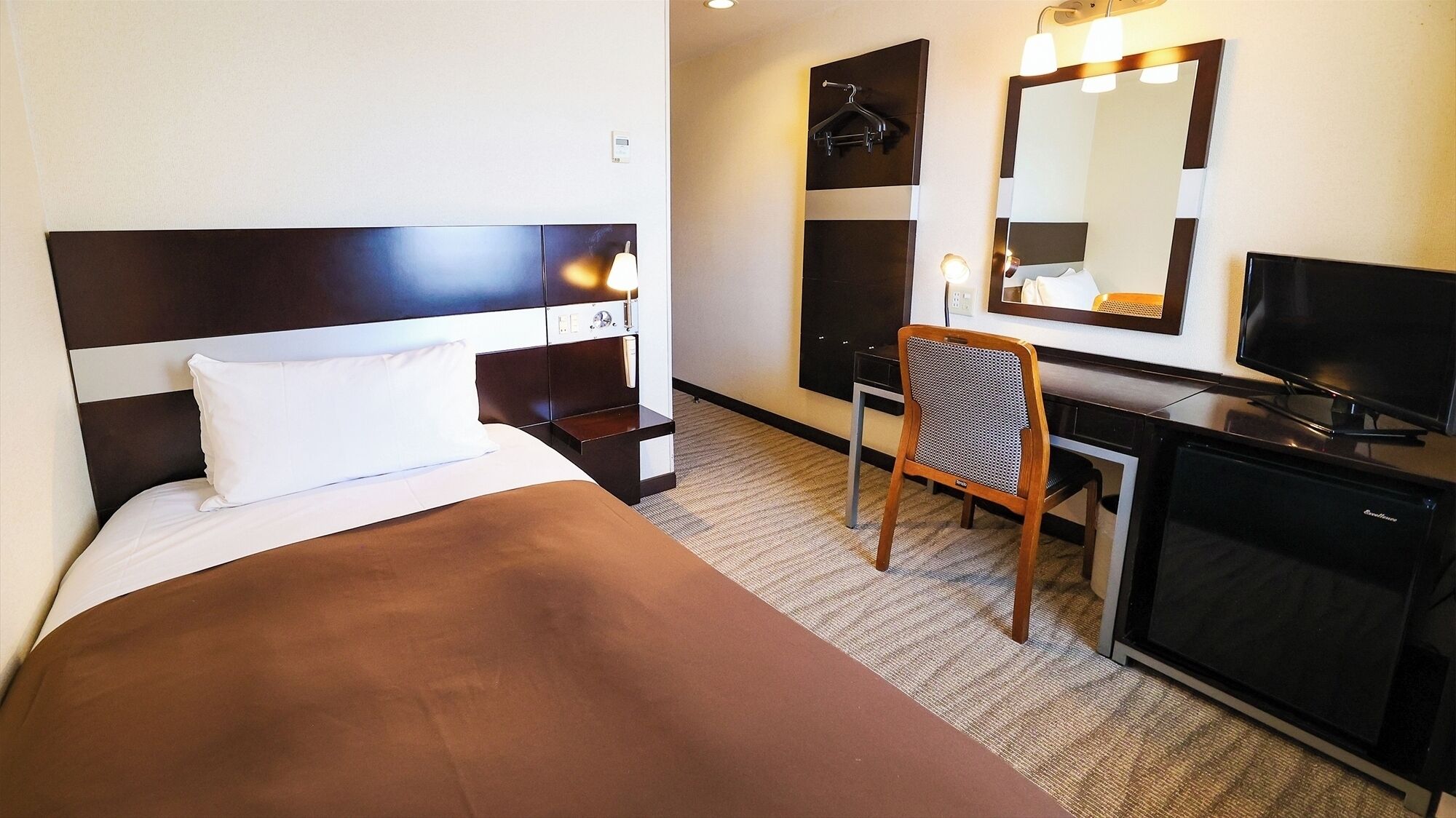 Ein Hotelzimmer mit Bett, Schreibtisch, Stuhl, Fernseher und Spiegel.