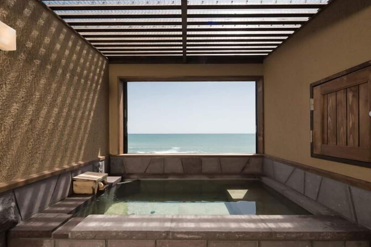 Un área de spa con vistas al océano, una puerta de madera y un muro de piedra.