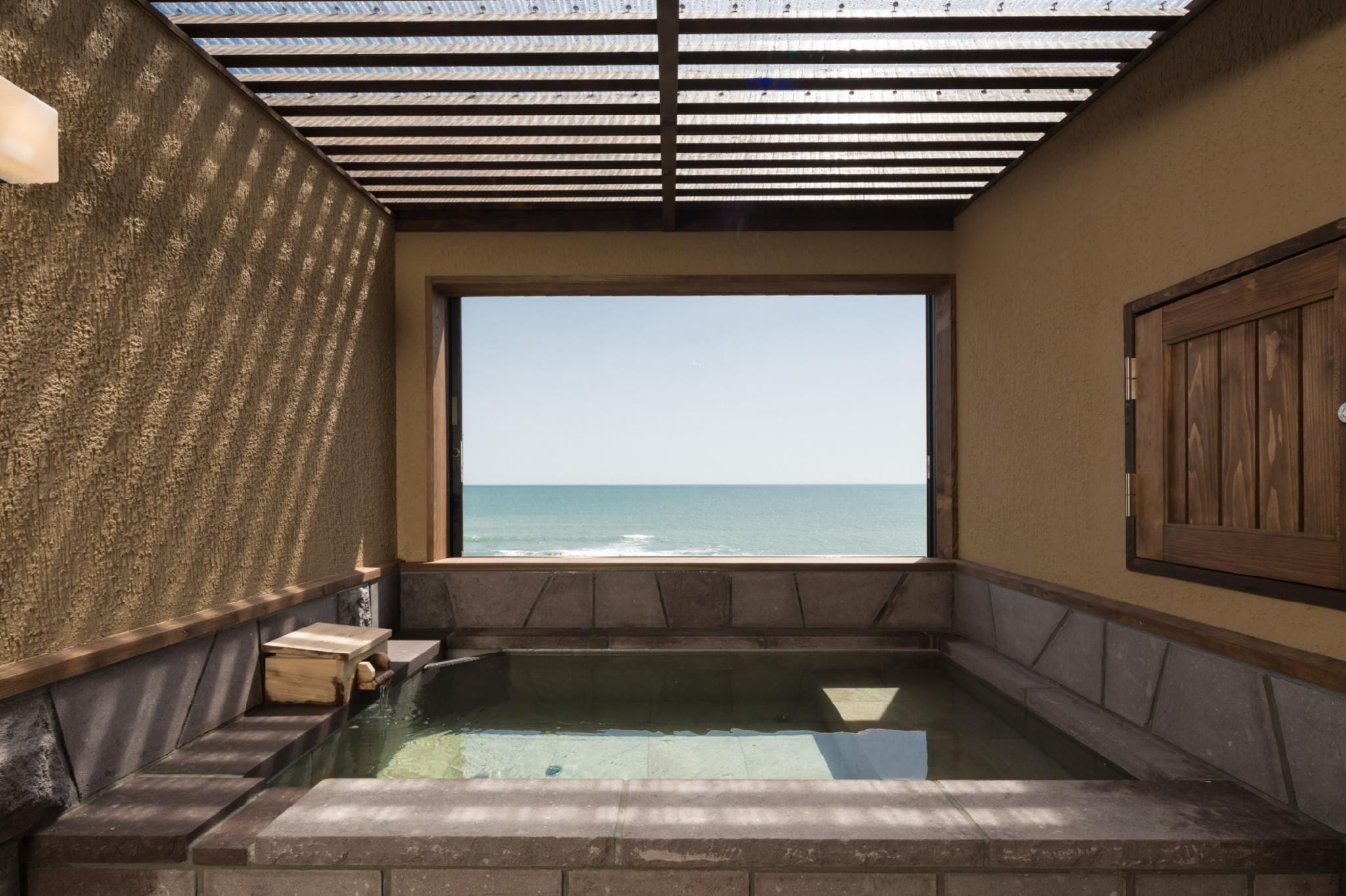A hot tub with a view of the sea, wooden walls, and a tiled floor.