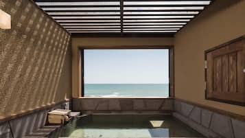 A hot tub with a view of the sea, wooden walls, and a tiled floor.