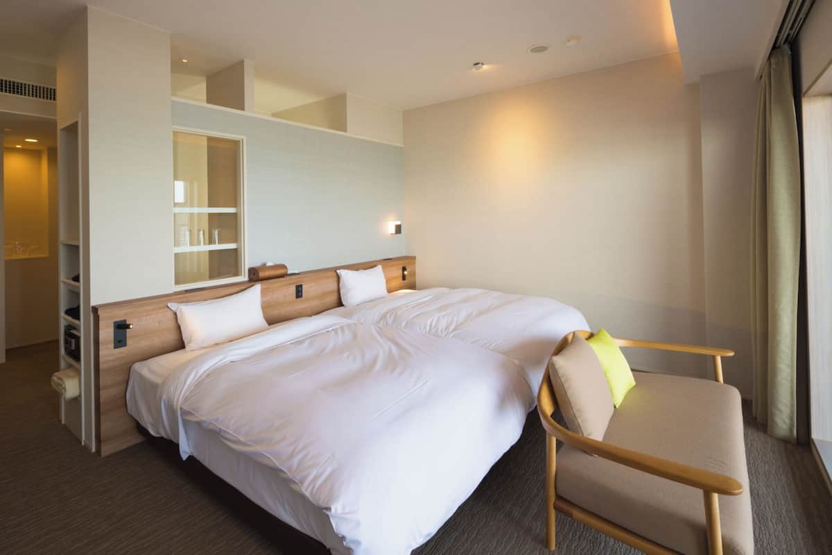 Una habitación de hotel con una cama grande, una mesita de noche, una silla, un armario y un espejo.