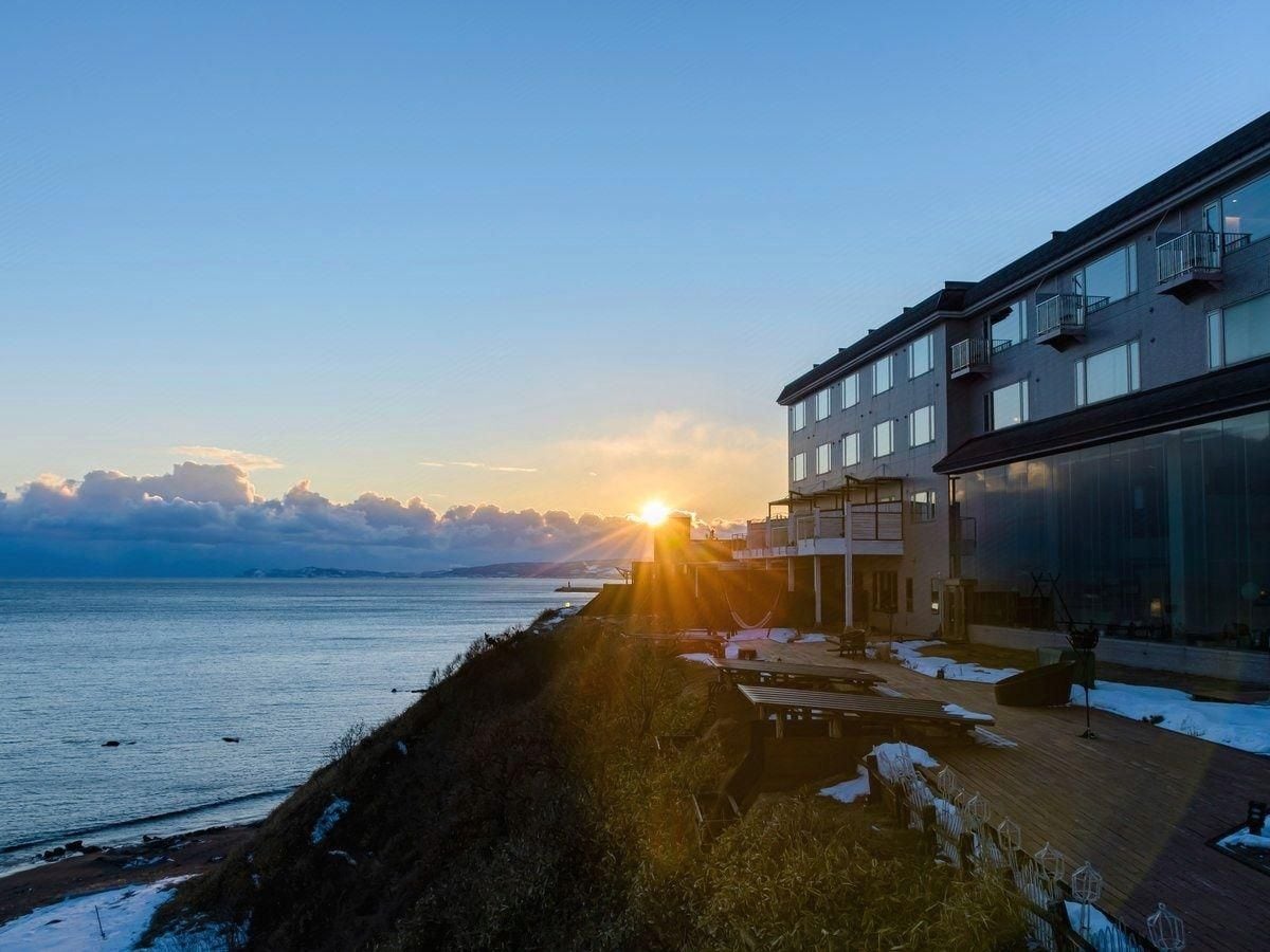 A coastal building with a balcony overlooking the sea, a wooden deck, and a clear sky.