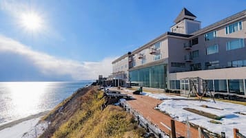A coastal hotel with a modern design, featuring a large glass facade, a rooftop deck, and a view of the sea.