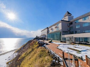A coastal hotel with a modern design, featuring a large glass facade, a rooftop deck, and a view of the sea. - Kokoronoresort Uminobetti Furukawa (Shiraoi)