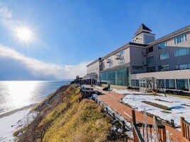 A coastal hotel with a modern design, featuring a large glass facade, a rooftop deck, and a view of the sea.
