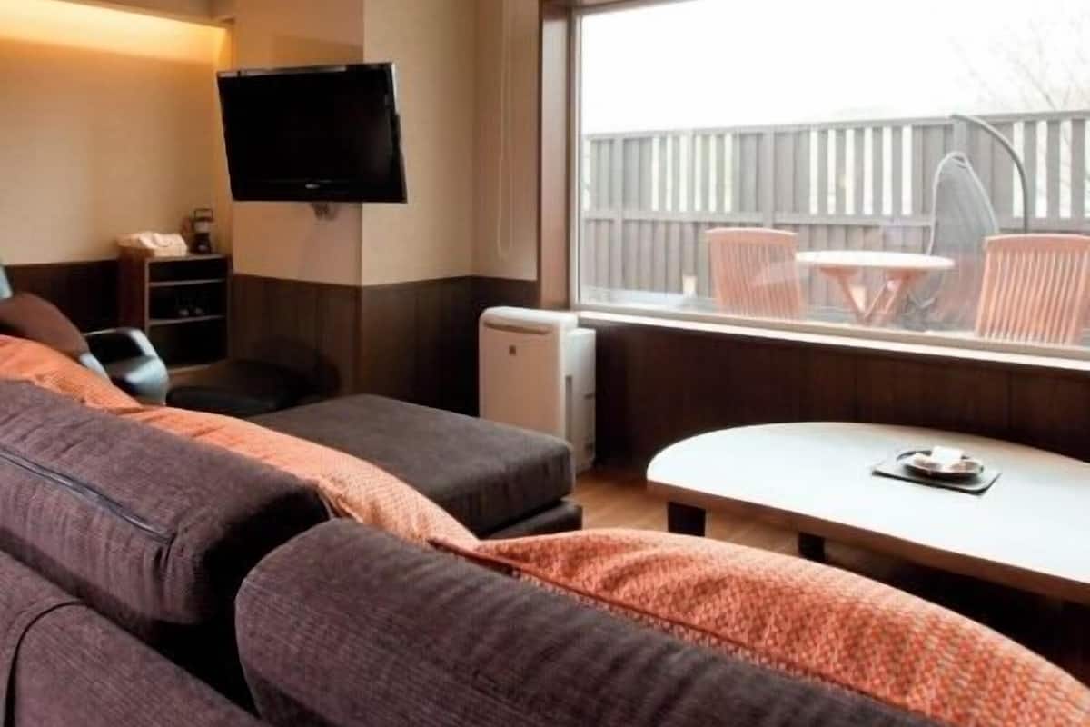 Una habitación de hotel moderna con sofá, una mesita, televisor montado en la pared y ventana con vistas a muebles de exterior.