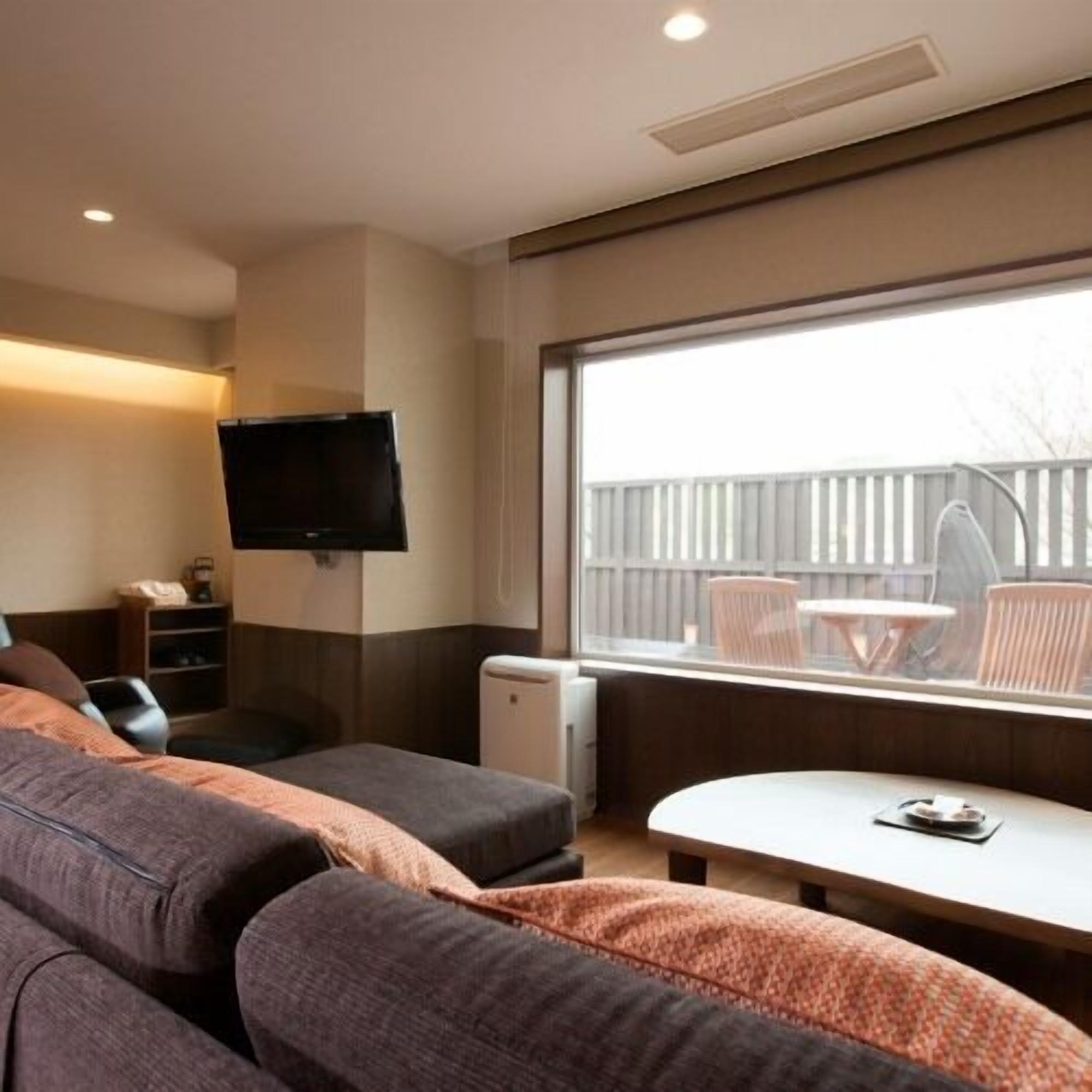 Una habitación con sofá, una mesita, televisor y ventana con vistas al exterior.