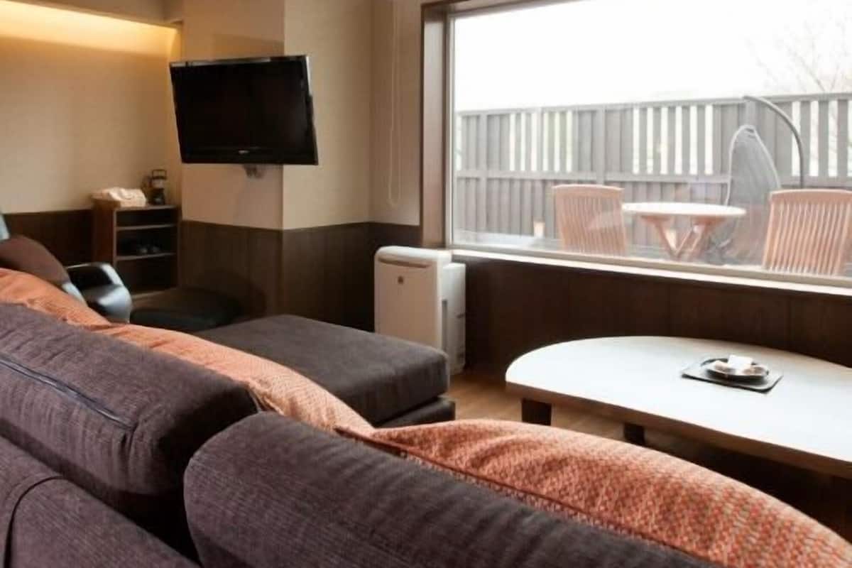 Una habitación con sofá, una mesita, televisor y ventana con vistas al exterior.