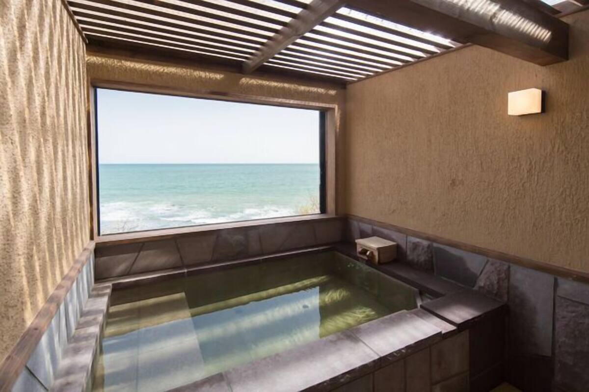 Un cuarto de spa con un amplio ventanal con vista al océano, un jacuzzi integrado y una pared de piedra.