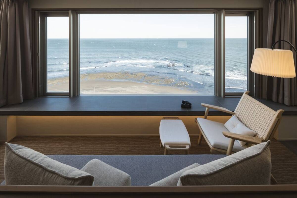 Una habitación con un amplio ventanal con vista al océano, un sofá, una silla y una lámpara.