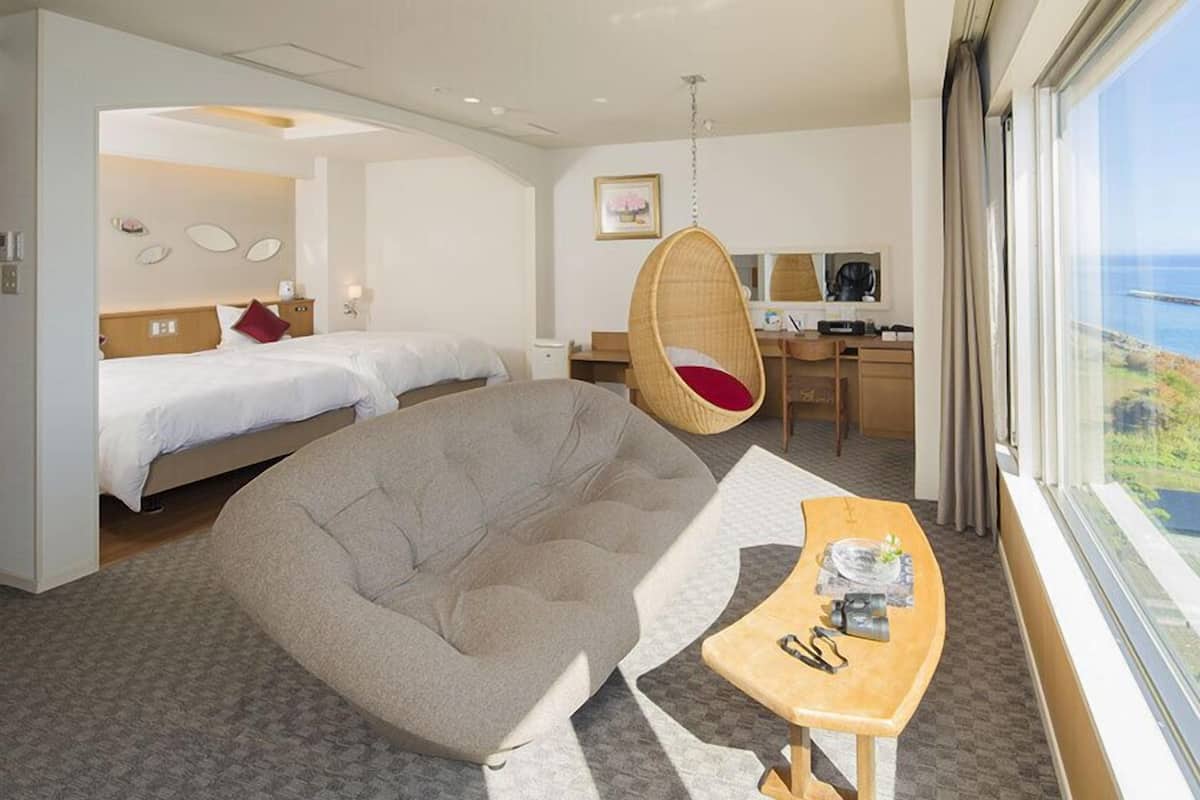 Habitación de hotel con sofá, dos camas, escritorio y vista al mar.