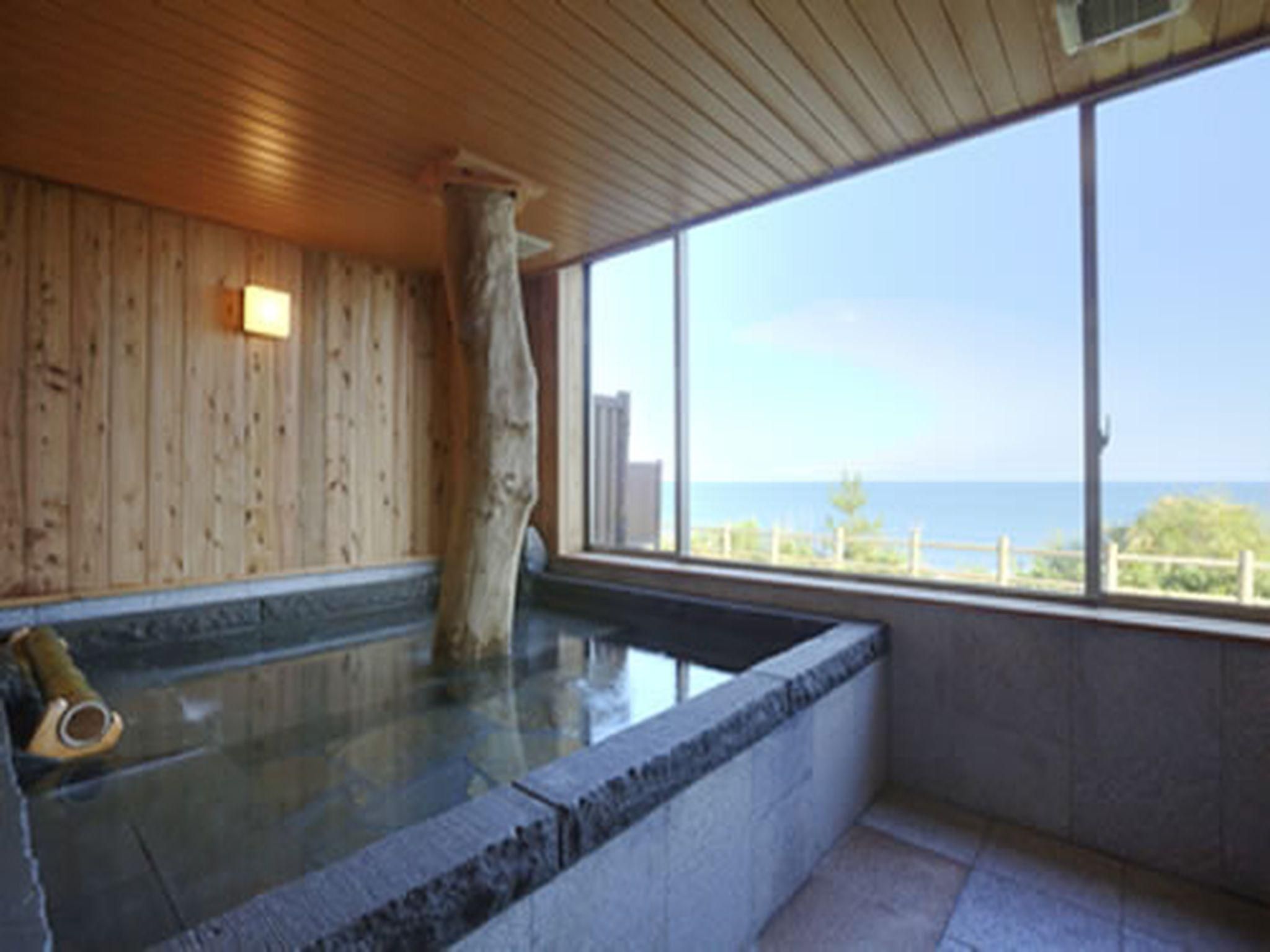 A wooden interior with a stone bathtub and a large window overlooking a body of water.