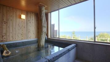 A wooden interior with a stone bathtub and a large window overlooking a body of water.