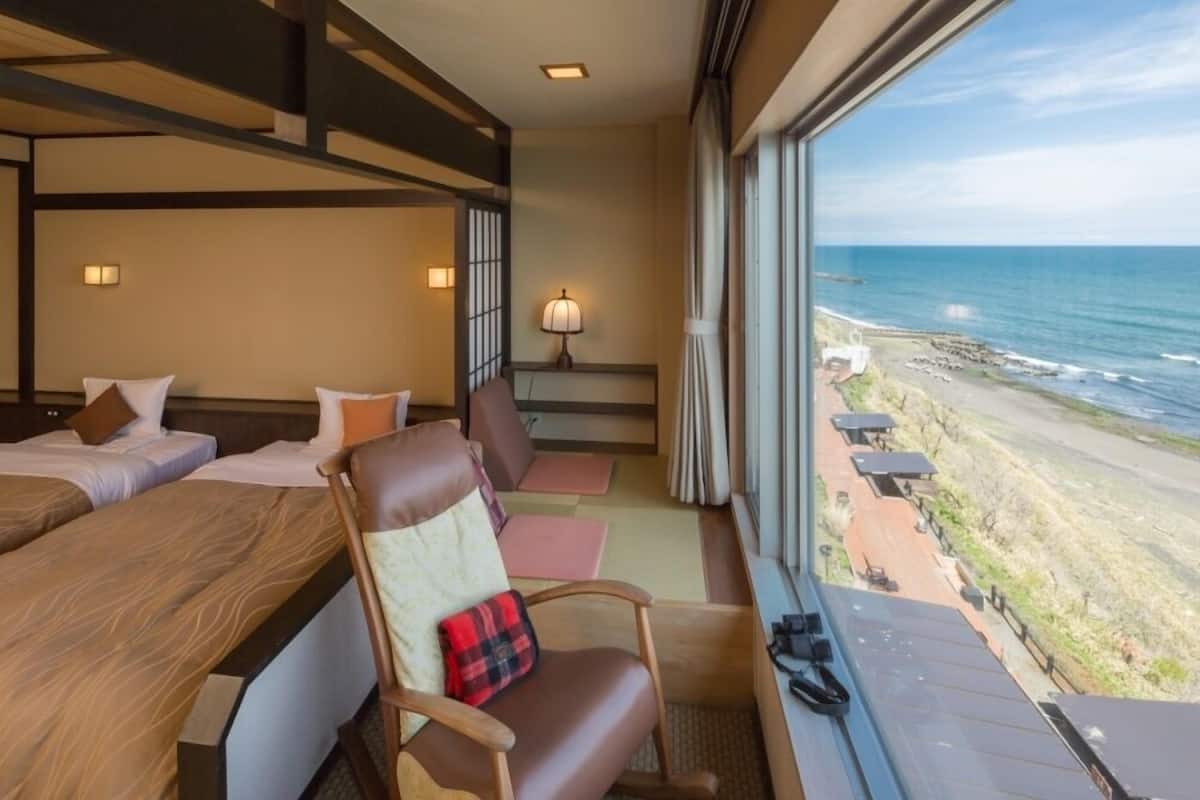 Habitación de hotel con balcón y vista a la playa, una cama, una silla y un escritorio con lámpara.
